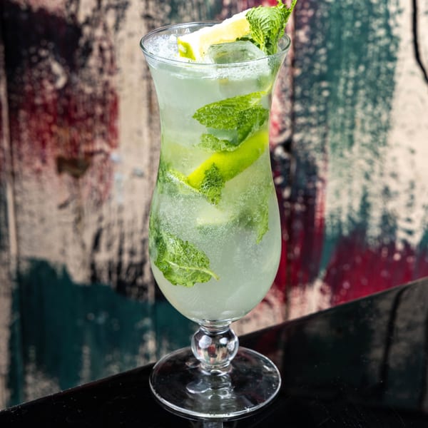 A refreshing mojito cocktail with mint leaves, lime wedges, and ice in a tall glass.