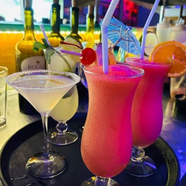 Three vibrant cocktails, two frozen pink drinks and one martini, on a dark tray at The Fish House.