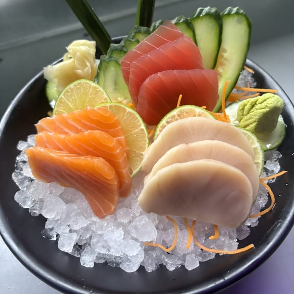 A seafood sashimi platter with salmon, tuna, and scallops, garnished with lime, cucumber, and ginger.