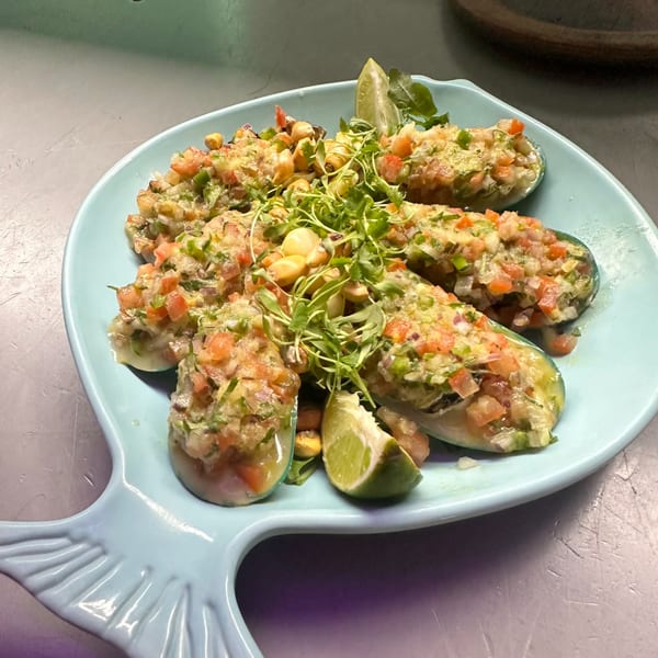 Mussels topped with pico de gallo, microgreens, and corn, served on a fish-shaped plate.