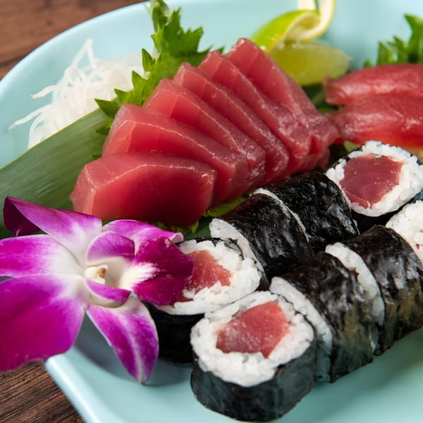 Fresh tuna sashimi and maki rolls, garnished with a purple orchid, on a light blue plate.