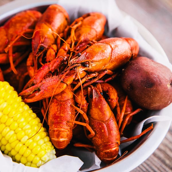 Boiled crawfish, corn on the cob, and a red potato in a metal bowl lined with white paper.