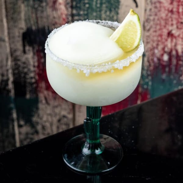 A frosty margarita with a salted rim and lime wedge in a green cactus-stemmed glass.