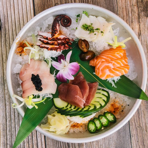 A seafood platter with octopus, salmon, tuna, and white fish, garnished with a purple orchid.