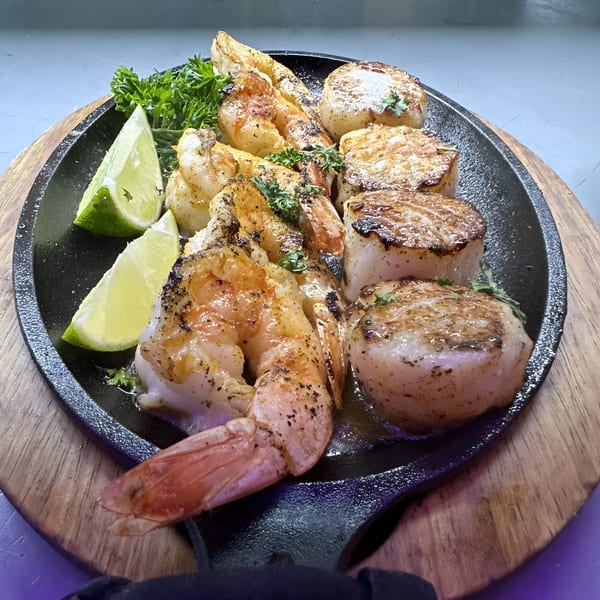 Sizzling shrimp and scallops with parsley and lime wedges on a cast iron skillet.