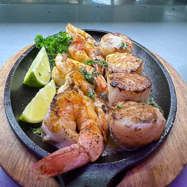 Sizzling platter of grilled shrimp and scallops, garnished with fresh parsley and lime wedges.