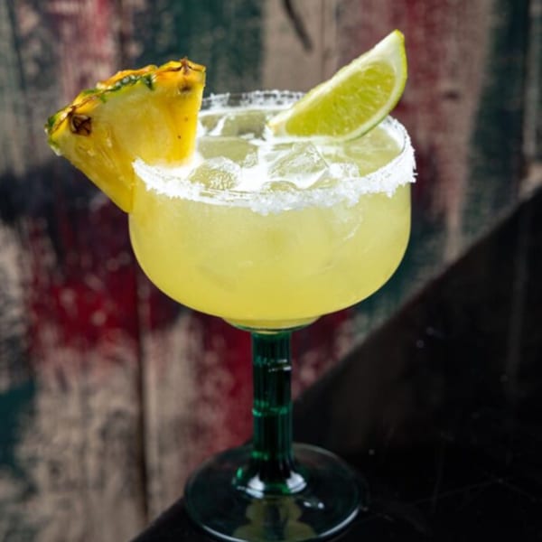 A pineapple margarita with a salted rim, garnished with a pineapple slice and lime wedge.